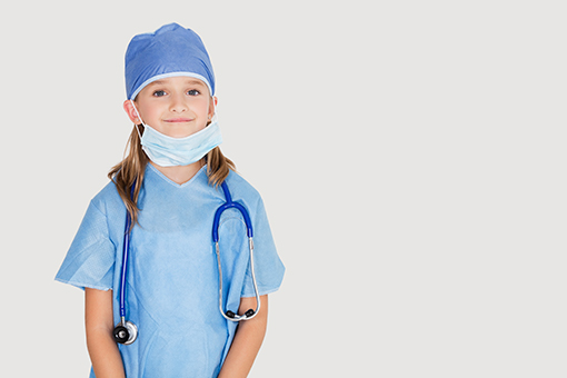 A young girl dressed as a medical professional with a scrub cap, mask, and stethoscope, smiling, on a light gray background.