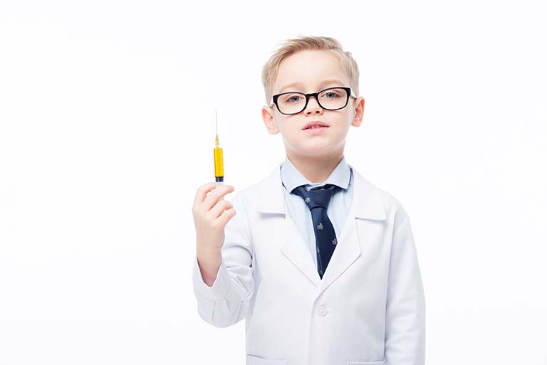 Young boy in glasses and lab coat holding a syringe, posing against a white background.